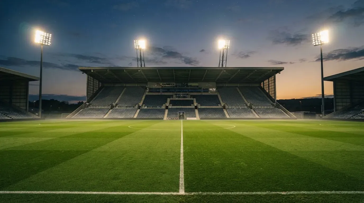 An empty football stadium with floodlight masts at dusk