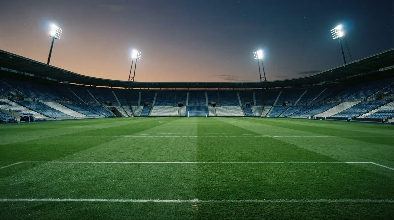 An empty football stadium with floodlight masts at dusk