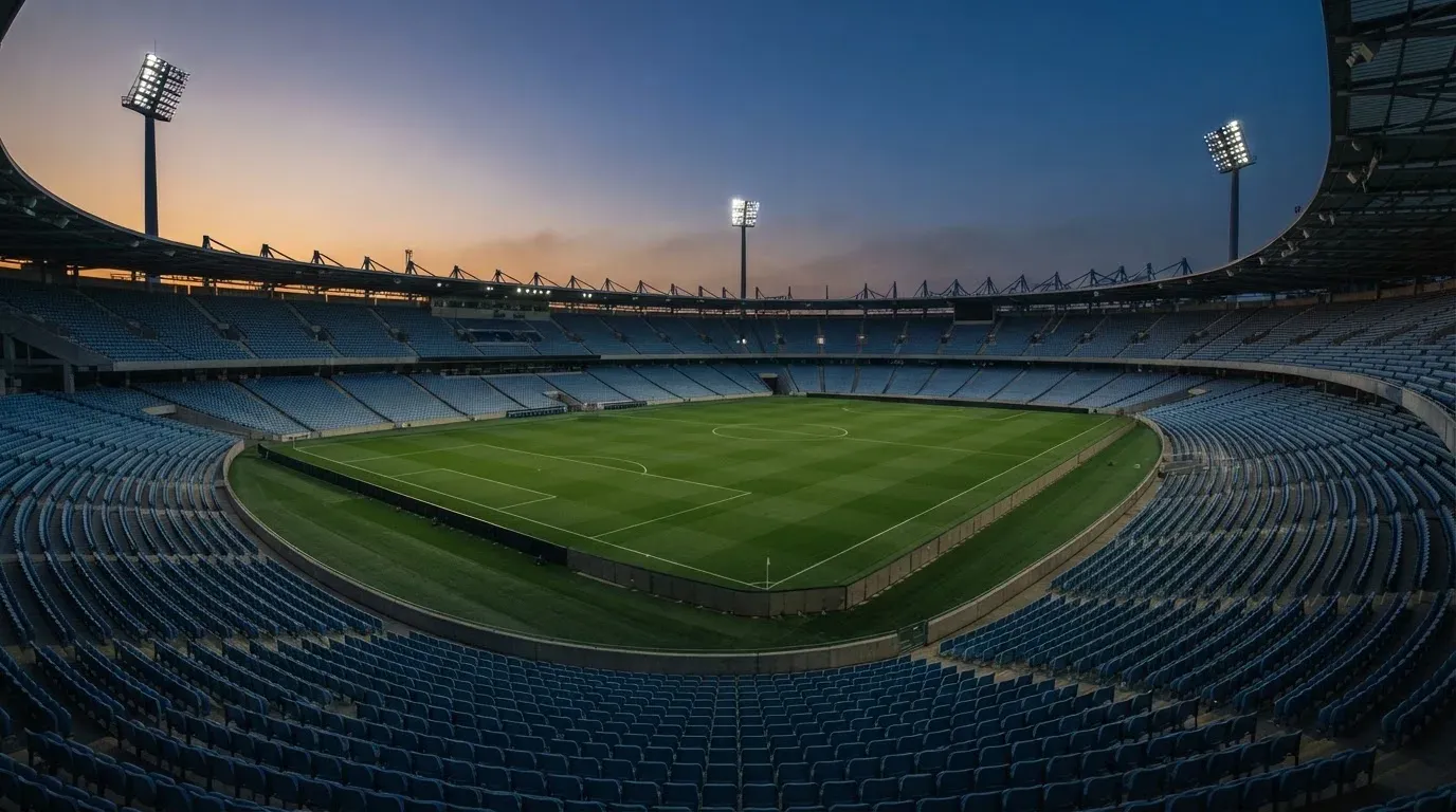 An empty football stadium with floodlight masts at dusk