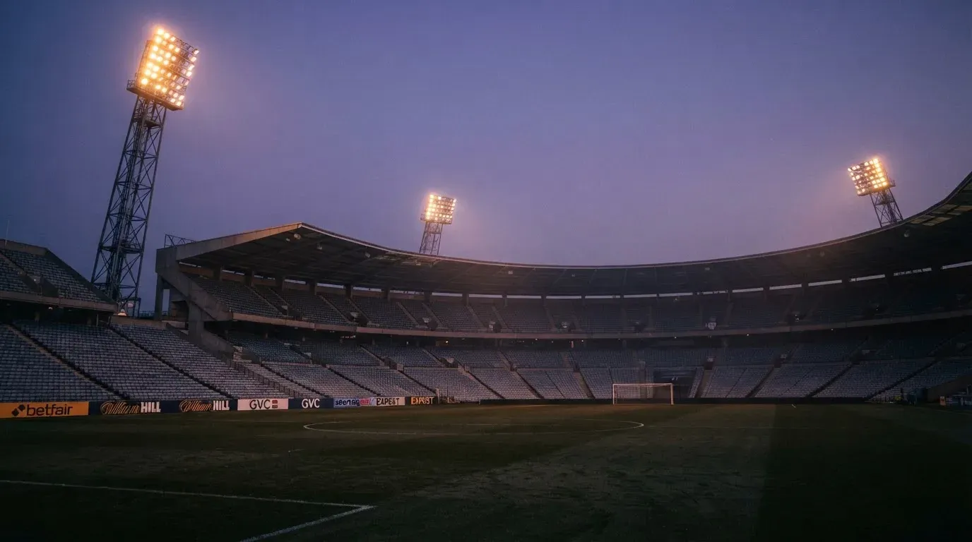 An empty football stadium with floodlight masts at dusk